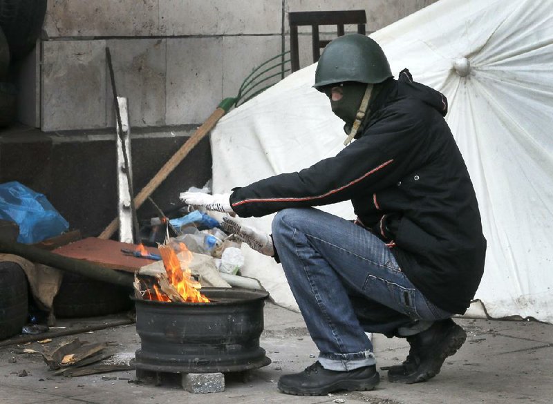 A masked pro-Russian activist warms himself next to a makeshift fire as he guards a regional administration building that they had seized earlier in Donetsk, Ukraine,  Friday, April 11, 2014.  Ukraine’s prime minister on Friday told leaders in the country’s restive east that he is committed to allowing regions to have more powers. Yatsenyuk Friday morning flew into Donetsk, where pro-Russian separatists are occupying the regional administration building and calling for a referendum that could prefigure seeking annexation by Russia. (AP Photo/Efrem Lukatsky)