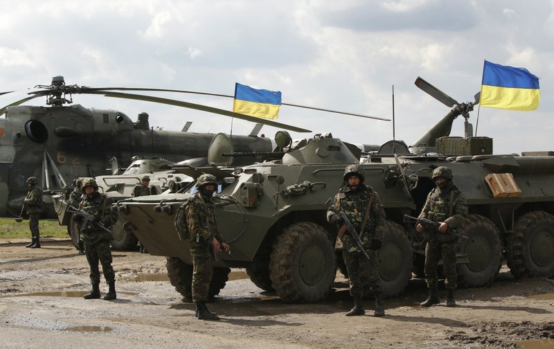 Ukrainian soldiers stand at armored personnel carriers, with Ukrainian flags in the back, as Ukrainian army troops receive ammunition in a field on the outskirts of Izyum, Eastern Ukraine, on Tuesday, April 15, 2014. An Associated Press reporter saw at least 14 armored personnel carriers with Ukrainian flags, one helicopter and military trucks parked 24 miles north of the city Tuesday.