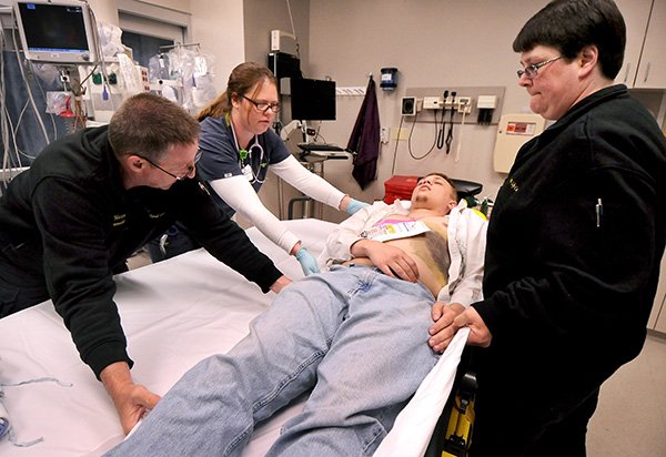 NWA Media/BEN GOFF 
Emergency room nurse Darcie Lee (second from left) helps paramedics Jeff Mason and his wife Missy Mason, owners and operators of Total Life Care private ambulance service in Garfield, move simulated patient Paul Bratcher, a nursing student at Northwest Arkansas Community College, from a stretcher to a bed Tuesday during a regional disaster preparedness drill at Northwest Medical Center-Bentonville.