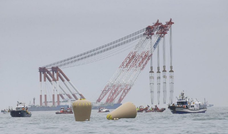 Cranes wait Friday near the buoys installed to mark the sunken ferry Sewol in the waters off the southern coast near Jindo, South Korea, after the last bit of the vessel’s blue keel disappeared. 