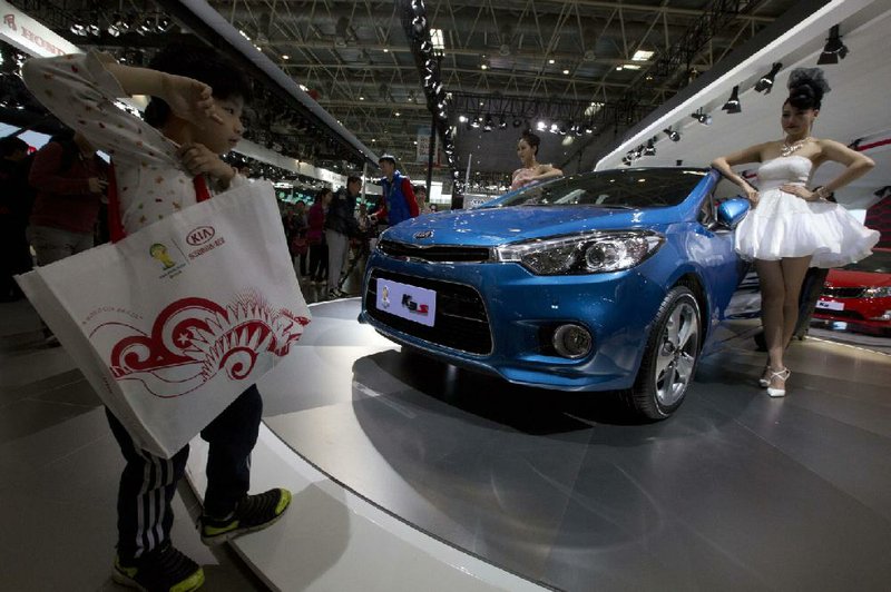 A young visitor walks near a car model posing next to a K3 sedan from Kia Motors displayed at the China Auto show in Beijing, China, Sunday, April 20, 2014. Automakers are looking to China's biggest auto show this year to help boost sales in this huge but cooling market. (AP Photo/Ng Han Guan)