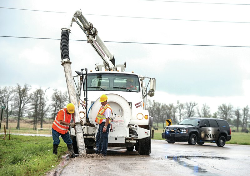 STAFF PHOTO ANTHONY REYES Nathan Walden, left, and Willy Alexander, both with the Huntsville Water Utilities, use an industrial vacuum truck to clean up human waste Monday along Klenc Road south of U.S. 412 in Tontitown. A truck from Jimmy Jones trucking in Berryville spilled the waste from the city of Huntsville while transporting it to the landfill. The cause of the spill is under investigation by the Arkansas Highway Police.