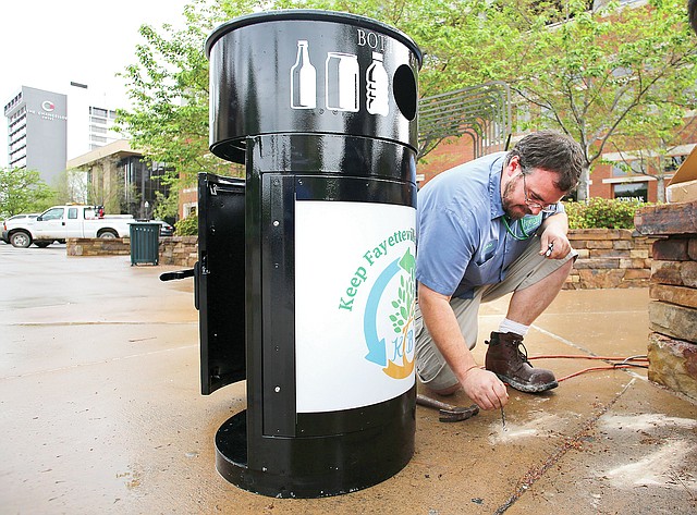 STAFF PHOTO DAVID GOTTSCHALK Sequoia Lansford, with the Fayetteville Recycling and Trash Collection Division, places bolts to secure a new recycling container for plastic, glass and cans Monday on the square in Fayetteville. Nine recycling containers are being placed on the square for use.