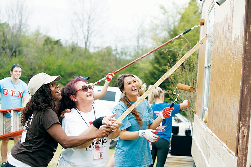 Shenel Sandidge, from left, executive director of Habitat for Humanity of Faulkner County; Suzanne Gonzalez, founder of Stand Together And No Drugs; and Molly Reed work together to remove a wasp nest so they can continue painting a mobile home in the Glen Echo mobile-home park in Conway during The Big Event.
