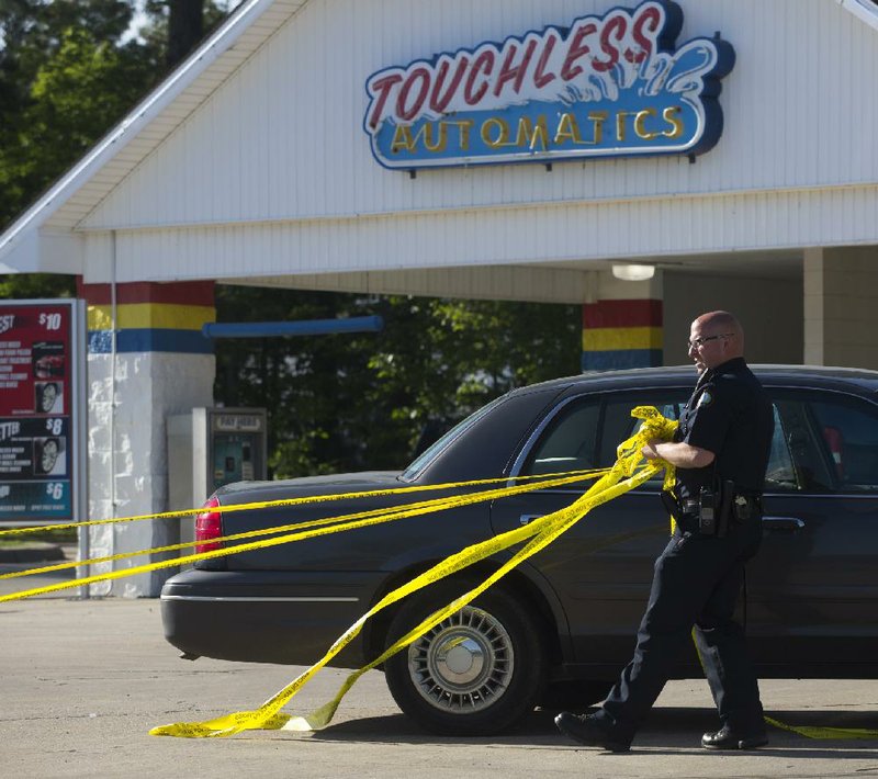 A Little Rock police officer removes crime-scene tape after an investigation into a triple shooting Friday at a Splash carwash on Baseline Road. 