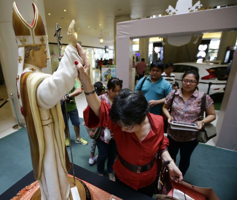 A devotee touches to pray at the statue of Roman Catholic Pope John Paul II on display with other relics of the late Pope as well as Pope John XXIII in celebration of their canonization or the elevation to sainthood Sunday, April 27, 2014, at suburban Quezon city, northeast of Manila, Philippines. Pope Francis declared his two predecessors John XXIII and John Paul II saints on Sunday before hundreds of thousands of people in St. Peter's Square, an unprecedented ceremony made even more historic by the presence of retired Pope Benedict XVI. The predominantly Roman Catholic Philippines joins several nations worldwide in the celebration of canonization of the two Popes. (AP Photo/Bullit Marquez)