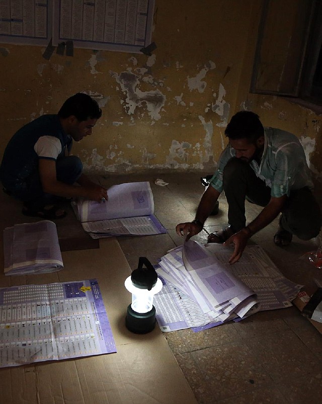 Electoral workers at a polling center in Baghdad count ballots Wednesday under lamplight after power was cut to the building. 