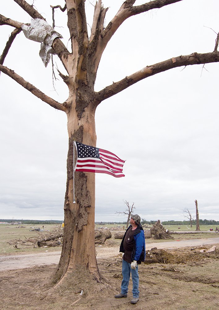 Preston Scroggin of Vilonia looks at the flag he had installed Monday after the April 27 tornado blew away his home, barn and outbuildings on what he calls the south farm, where he has lived since 1980. Scroggin said the flag makes the statement that Vilonia is strong and will rise again. The tree was one of only three of his that survived the April 25, 2011, tornado, he said, but the tree was heavily damaged this time. Scroggin, a former Faulkner County judge, is director of the Arkansas Livestock and Poultry Commission.