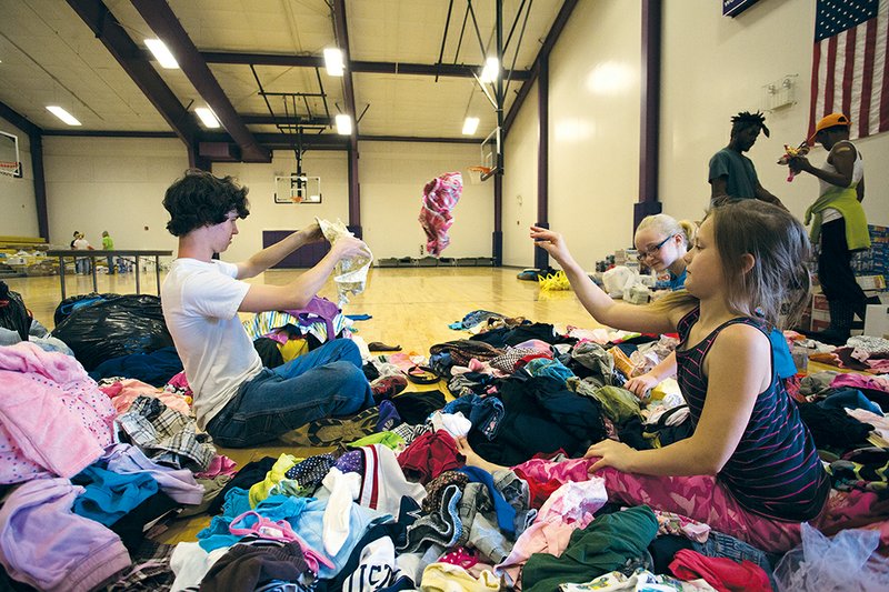 Students Ben Deierlein, 15, clockwise from left, a Mayflower High School student; Zoey Patterson, 10, a Vilonia Primary School student; and Lily Dycus, 9, a Mayflower Elementary School student, sort and fold clothes in the Mayflower Middle School gymnasium.