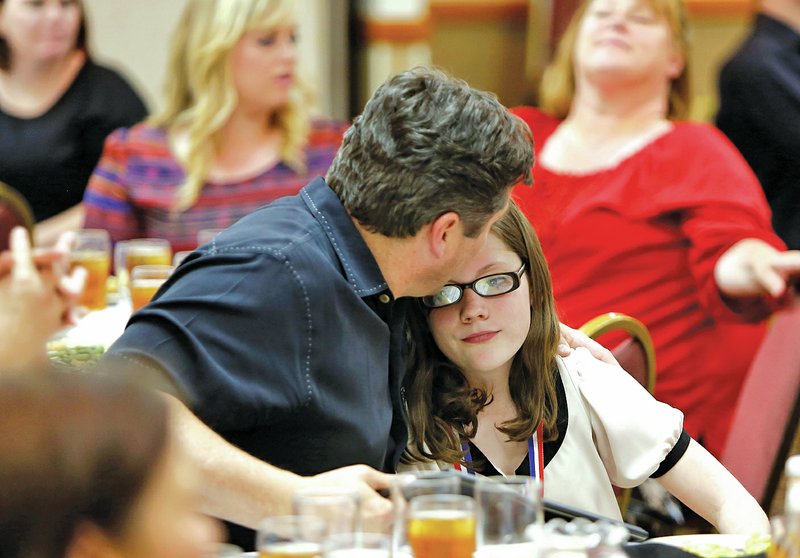 STAFF PHOTO DAVID GOTTSCHALK Doug Walker, left, gives daughter Annie Walker, 12, of McNair Middle School, a hug and kiss after returning to her table after receiving a medal and awards from the Fayetteville Sequoyah Kiwanis.
