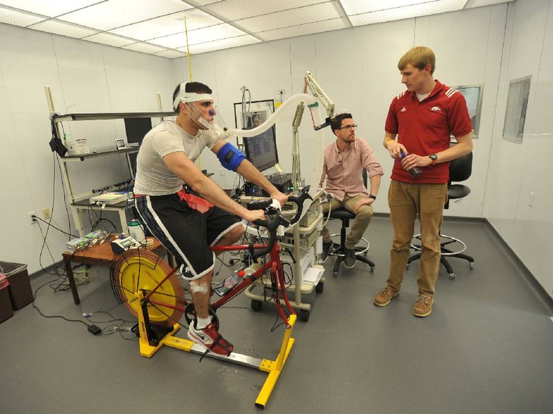 Student athlete Kikko Haydar works out in the new environmental chamber at the University of Arkansas HPER building Wednesday afternoon as UA students Matt Tucker and J.D. Adams (right) check his vital statistics during a demonstration for the grand opening in Fayetteville. The chamber can be controlled to study the effects of heat and hydration on the body. 