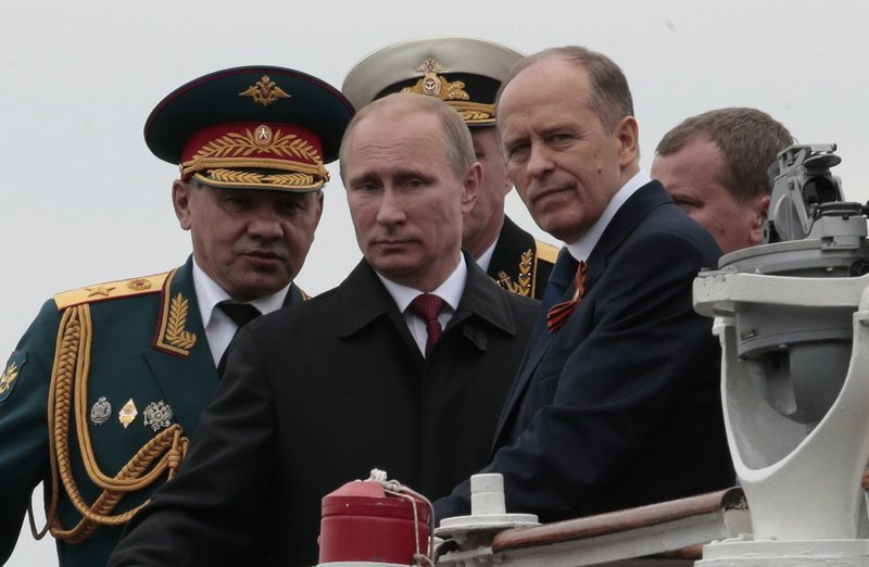 Russian President Vladimir Putin, flanked by Defense Minister Sergei Shoigu, left, and Federal Security Service Chief Alexander Bortnikov, right, arrives on a boat after inspecting battleships during a navy parade marking the Victory Day in Sevastopol, Crimea, on Friday, May 9, 2014. 