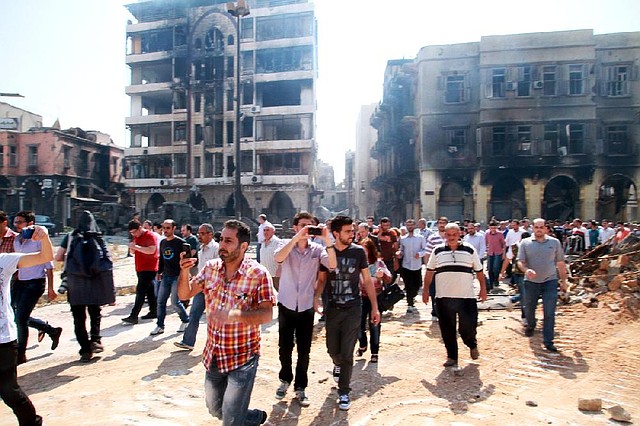 In this photograph made on a government-led media tour, Syrian civilians return to Homs, Syria on Friday, May 9, 2014, where bulldozers cleared rubble from the streets of battle-scarred districts in the central Syrian city after government troops entered the last rebel-held neighborhoods as part of an agreement that also granted opposition fighters safe exit from the city. (AP Photo)