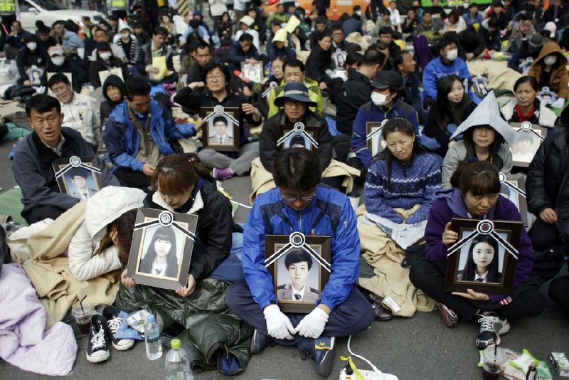 Family members holding the portraits of the victims of the sunken ferry Sewol, sit on a street near the presidential Blue House in Seoul, South Korea, Friday, May 9, 2014. Family members marched to the presidential Blue House in Seoul early Friday calling for a meeting with President Park Geun-hye but ended up sitting on streets near the presidential palace after police officers blocked them. Park's office said a senior presidential official plans to meet them later Friday. (AP Photo/Lee Jin-man)
