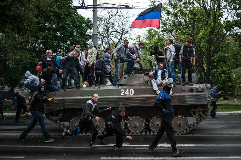 People with the Donetsk republic flag stand atop a Ukrainian government forces armored personal carrier seized by pro-Russia insurgents during fighting in Mariupol, eastern Ukraine, Friday, May 9, 2014. In Ukraine's east, where pro-Russia insurgents have seized government buildings and fought with Ukrainian forces, fatal fighting broke out in the city of Mariupol.  Ukrainian Interior Minister Arsen Avakov said about 60 gunmen attacked the police station and were repelled in an operation that killed one policeman and about 20 people that he called “terrorists.”   (AP Photo/Evgeniy Maloletka)