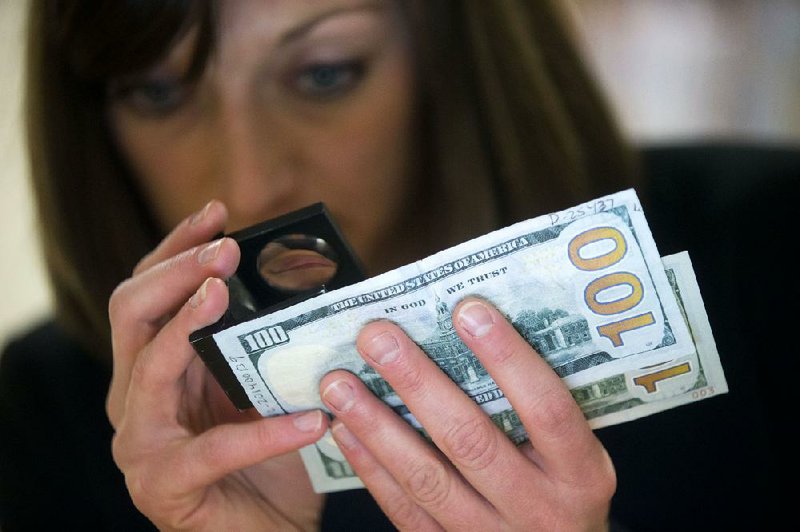 Marybeth Dellibovi, counterfeit specialist with the U.S. Secret Service, demonstrates comparing a genuine bank note to a counterfeit bank note in the counterfeit specimen vault room at the Secret Service headquarters in Washington, D.C., U.S., on Wednesday, March 12, 2014. The Federal Reserve began supplying banks in October with a redesigned $100 note with features aimed at thwarting counterfeiters, including a blue, three-dimensional security ribbon with images of bells and 100s. Photographer: Andrew Harrer/Bloomberg *** Local Caption *** Marybeth Dellibovi