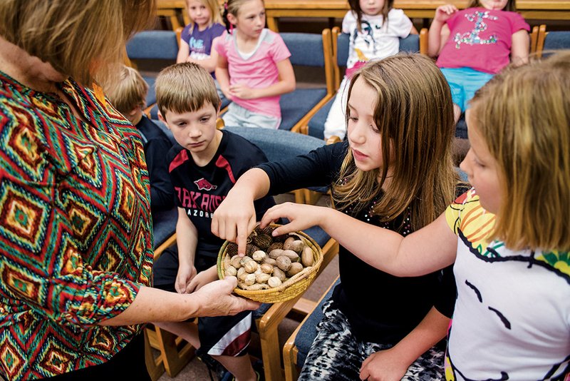 Janice Fisher, left, president of the Ouachita Chapter of the Arkansas Archaeological Society, shows Magnet Cove students, from left, Hayden Browning, Mia Harper and Layla Ault a variety of nuts that would have been part of the diet for Native Americans.
