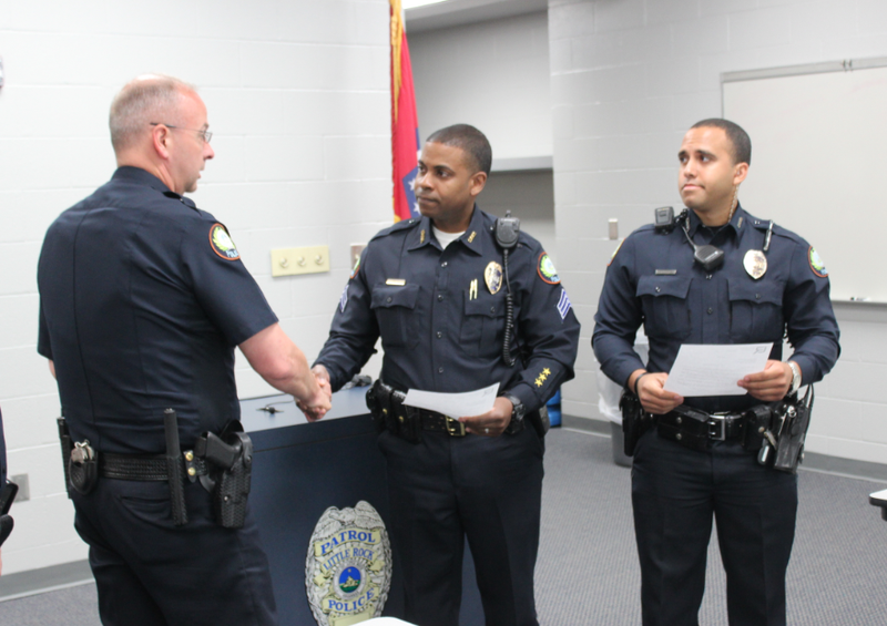 Little Rock Police Department Capt. Ty Tyrrell, left, shakes hands with Sgt. Brian Grigsby on Thursday after presenting letters of commendation to Grigsby and officer Troy Dillard, right, for their work in finding a missing man and then helping him buy Mother's Day flowers for his wife.