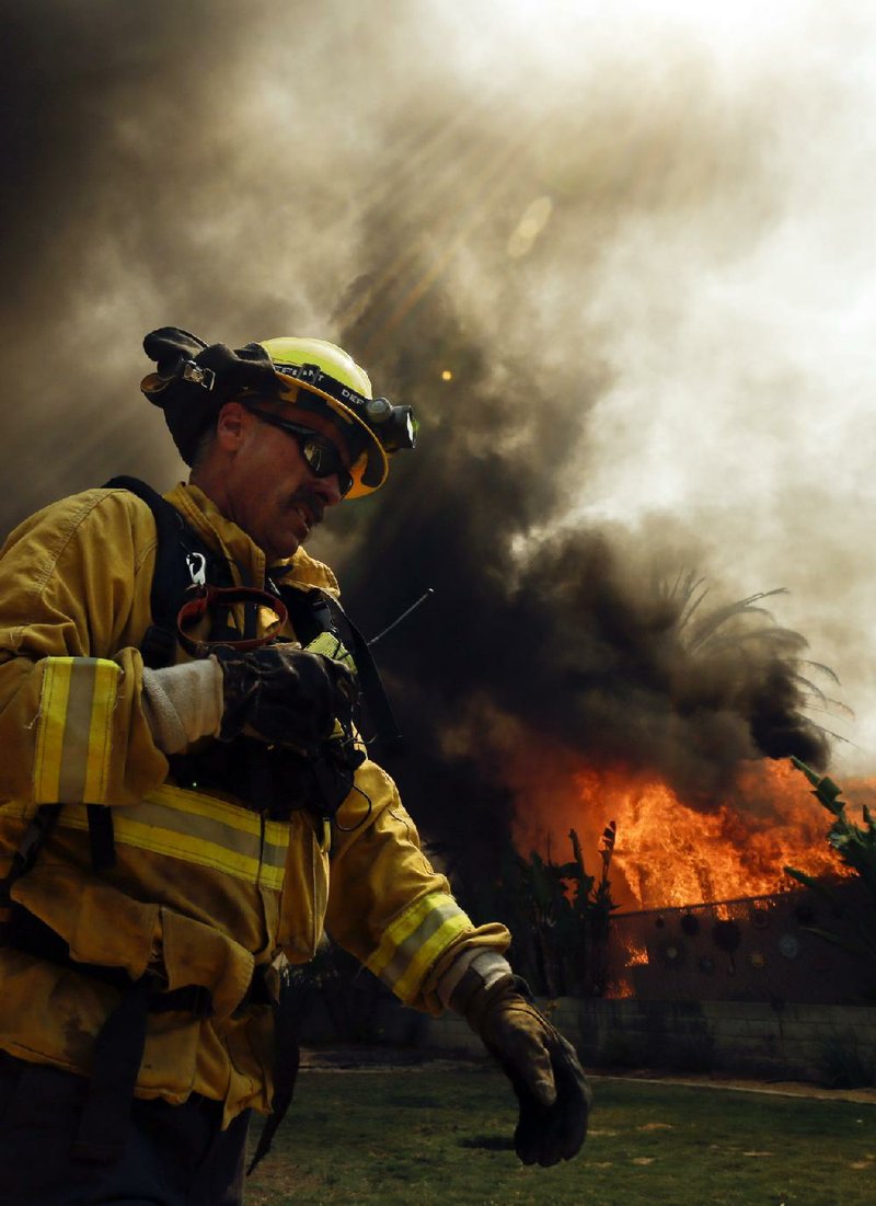 A firefighter moves past a burning structure Thursday in Escondido, Calif. Dry conditions and hot weather are fueling nine wildfires in San Diego County. 