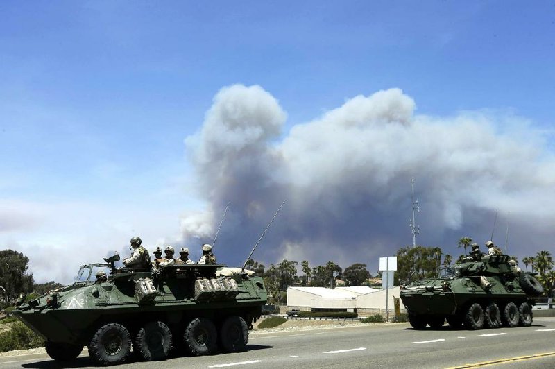 Marines move military vehicles near the entrance to California’s Camp Pendleton as smoke billows Friday from a wildfire on the base. 