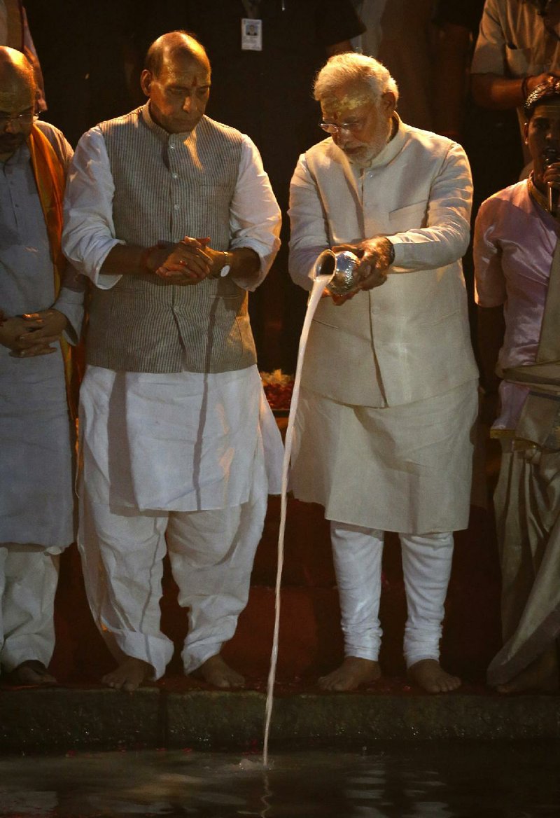 Hindu nationalist Bharatiya Janata Party (BJP) leader and India's next prime minister Narendra Modi performs evening rituals, with BJP President Rajnath Singh, second left, and Amit Shah, left, standing on the banks of the River Ganges in Varanasi, an ancient city revered by millions of devout Hindus, India, Saturday, May 17, 2014. Modi will be India's next prime minister, winning the most decisive victory the country has seen in more than a quarter century and sweeping the long-dominant Congress party from power, results showed Friday. An elaborately decorated platform was built for him to offer prayers on the banks of the river. Saffron flags fluttered above the flower bedecked platform and thousands of supporters and onlookers milled around to watch as Hindu priests chanted sacred verses and burnt incense. (AP Photo/Saurabh Das)