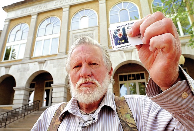 STAFF PHOTO BEN GOFF Horace Crosby holds up his new Arkansas voter identification card Friday in front of the Benton County Courthouse in Bentonville. Crosby, who recently made Highfill his permanent residence and still has an out-of-state driver&#8217;s license, says he experienced numerous delays in obtaining suitable identification to vote in Arkansas.
