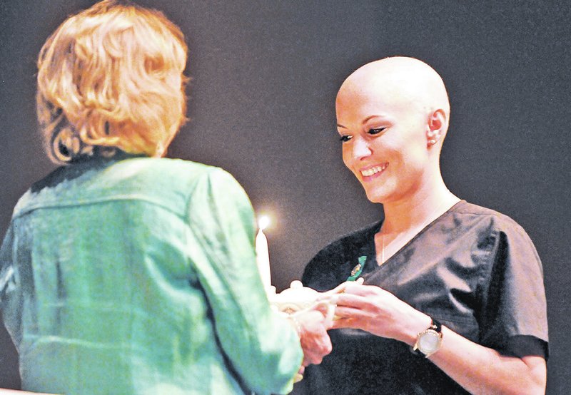 STAFF PHOTO BEN GOFF Abby Kolb-Selby, left, lights Amber Miller&#8217;s lamp Saturday as part of the NorthWest Arkansas Community College Nursing Pinning Ceremony for the class of May 2014 in the Arend Arts Center at Bentonville High School. Miller, who is undergoing chemotherapy, surprised everyone by removing her wig after stepping forward to receive her pin during the service.