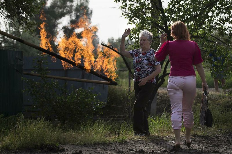Local residents talk to each other as they look at flame from a damaged gas pipe after an impact of a mortar bomb, during fighting between Ukrainian government troops and pro-Russian militants, outside Slovyansk, eastern Ukraine, early Monday, May 19, 2014. Lawmakers and officials from eastern Ukraine on Saturday poured criticism on the fledging central government, accusing it of ignoring legitimate grievances of the regions which have been overrun by pro-Russia militia fighting for independence. (AP Photo/Alexander Zemlianichenko)