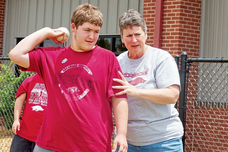 Caleb Cook, left, gets some pointers from Special Olympics Arkansas Director Sally Paine before practicing throwing a softball in preparation for the summer games.
