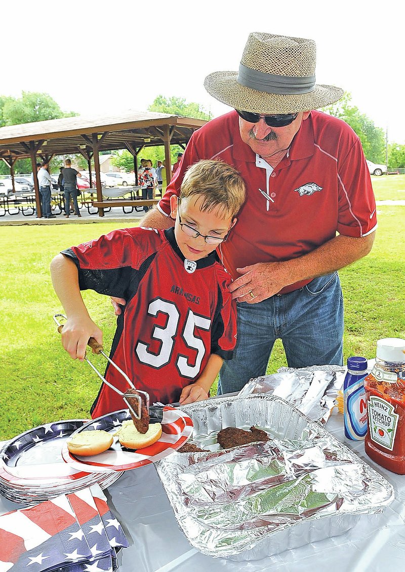 STAFF PHOTO FLIP PUTTHOFF Larry Smith, Cave Springs mayor, helps Joe Yount, 12, at left, get the food line started Friday at a dedication of the remodeled Cave Springs City Park. The park was redone to add a playground, restroom building, basketball court, fencing and other improvements. Smith said the project cost $130,000 but most of the money came from grants. Less than $10,000 in city money was spent, Smith added. A cookout Friday helped celebrate the project&#8217;s completion.