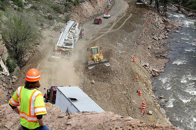 In this May 20, 2014 photo, Colorado Department of Transportation engineer Abra Geissler watches as a dozer moves dirt and traffic is escorted along what will eventually be an improved mountain highway, during a road-building operation on Highway 36 between Lyons at Estes Park, Colorado. The goal of the project is to move the road further from the adjacent river, which undermined the road for miles during floods the previous fall, in hopes of preventing such destructive flooding in the future. (AP Photo/Brennan Linsley)