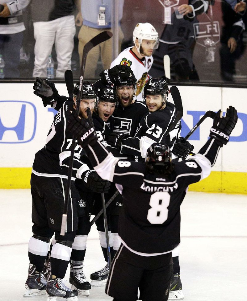 Los Angeles Kings' Jeff Carter (77), Tyler Toffoli (73), Jake Muzzin (6), Dustin Brown (23) and Drew Doughty (8) celebrate a goal by Muzzin as Chicago Blackhawks' Jonathan Toews skates behind them during the first period of Game 4 of the Western Conference finals of the NHL hockey Stanley Cup playoffs on Monday, May 26, 2014, in Los Angeles. (AP Photo/Jae C. Hong)