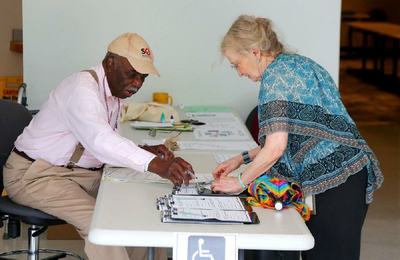 Election official Leonard Johnson at the Pulaski County Regional Building at 501 W. Markham in Little Rock assists Carol Silverstrom as she prepares to vote early for Tuesday’s runoff election. Early voting continues at that location until Monday. 