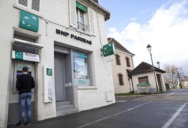 A customer uses an ATM at a branch of BNP Paribas SA bank in Jouars-Pontchartrain, France, in this February photo. The bank says it faces fines of more than the $1.1 billion it set aside in response to a U.S. investigation of its currency transactions.
