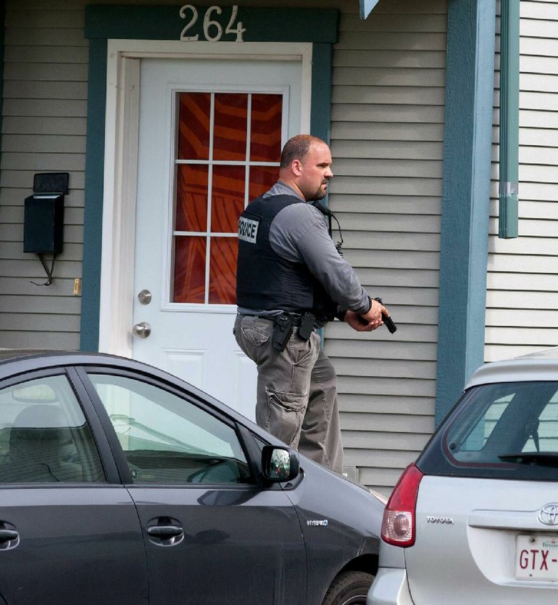 A Royal Canadian Mounted Police officer searches around a house in Moncton, New Brunswick, on Thursday in the hunt for a heavily armed gunman suspected of killing three Mounties and injuring two others.