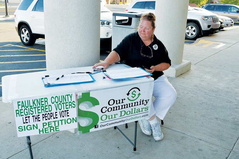 A woman who is an employee of National Ballot Access and declined to give her name mans a table outside Walgreens on Oak Street in downtown Conway. She was gathering signatures for the Our Community, Our Dollars campaign, which seeks about 25,000 signatures in Faulkner County to get the wet-dry issue on the Nov. 4 ballot. The Decline to Sign Campaign is working against the effort.