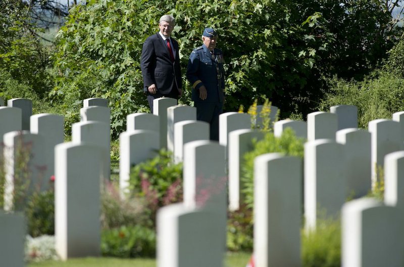 Canadian Prime Minister Stephen Harper speaks with Major-General Richard Rohmer as he walks through the Canadian military cemetery Friday, June 6, 2014, in Beny-sur-Mer, France. 