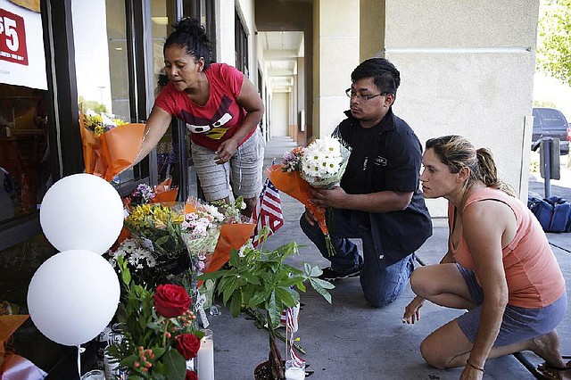 Sandra Flores (from left), Jonathan Solano and Leticia Trejo place flowers in front of a CiCi’s Pizza on Monday in Las Vegas. People have begun to create a makeshift memorial in front of the restaurant where two Las Vegas Metropolitan Police officers were killed.