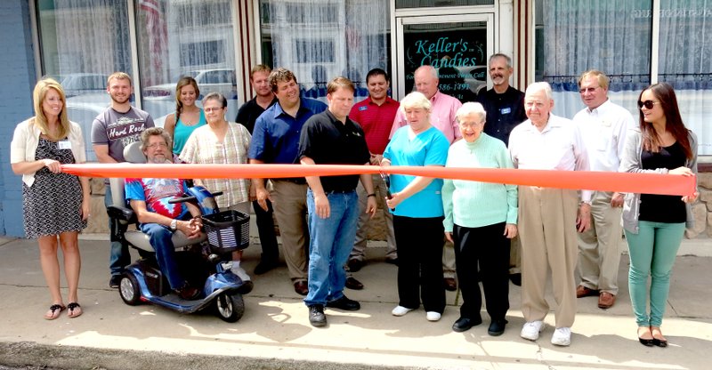 Photo by Mike Eckels With members of the Gravette Chamber of Commerce in the background, civic leaders help Julene Stout cut the ribbon, formally opening Keller&#8217;s Candies on May 29 in downtown Gravette. Amanda Sittlein (far left) and Morgan Black (far right) hold the ribbon while Mike Von Ree (left), Mayor Bryon Warren, Chamber president Kurt Maddox, Julene Keller Stout, Vivian Keller and Bill Keller cut the ribbon.