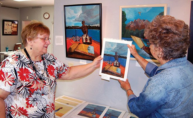 Artist and Arkadelphia Arts Center volunteer Dolores Middleton, left, joins Arts Center Director Farrell Ford to look over some prints and original paintings by Clark County painter Sam Blackmon that are on display and for sale at the arts center on Main Street in downtown Arkadelphia.