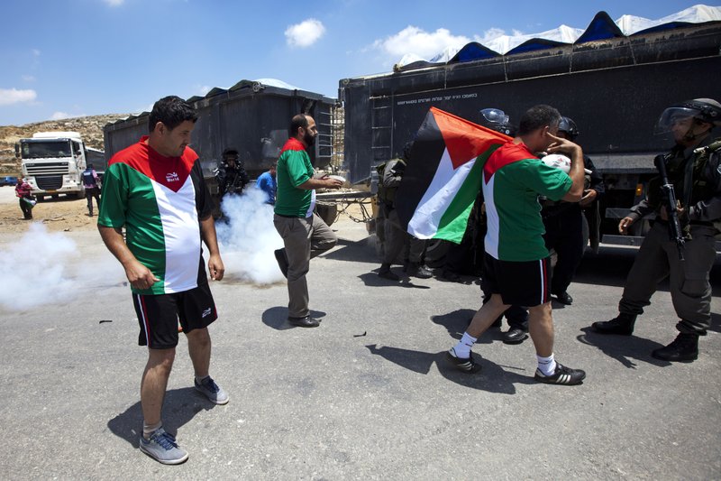 Israeli border policeman and Palestinian protesters argue during a demonstration in support for dozens of Palestinian hunger strikers in Israeli jails, outside Ofer military prison, near the West Bank city of Ramallah, Wednesday, June 11, 2014. A day before the start of the World Cup in Brazil, protesters dressed up in the jerseys of the Palestinian football team and kicked a ball around outside Ofer, an Israeli lockup in the West Bank. A group of helmeted soldiers prevented them from advancing. Troops fired stun grenades and pushed some of the players who dribbled and kicked the ball over the heads of soldiers.