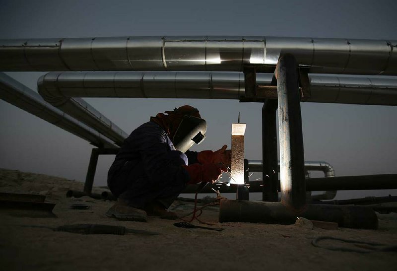 An welder works on a pipeline in the desert oil fields of Sakhir, Bahrain, at sunset on Tuesday. OPEC’s oil ministers voted Wednesday to maintain a production target of 30 million barrels a day.