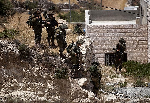 Israeli soldiers conduct a military operation to search for three missing teenagers outside the West Bank city of Hebron, Monday, June 16, 2014. Israeli troops on Monday rounded up dozens more senior Hamas activists and killed a Palestinian in a clash with stone throwers — part of a feverish search for three kidnapped Israeli teenagers who Israel alleges were seized by the Islamic militant group. (AP Photo/Majdi Mohammed)