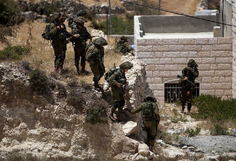 Israeli soldiers conduct a military operation to search for three missing teenagers outside the West Bank city of Hebron, Monday, June 16, 2014. Israeli troops on Monday rounded up dozens more senior Hamas activists and killed a Palestinian in a clash with stone throwers — part of a feverish search for three kidnapped Israeli teenagers who Israel alleges were seized by the Islamic militant group. (AP Photo/Majdi Mohammed)