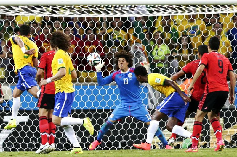 Mexican goalkeeper Guillermo Ochoa (13) bats away a header by Brazil’s Fred (left) during a Group A match Tuesday in Fortaleza, Brazil. Ochoa stopped all eight Brazilian shots as the teams battled to a 0-0 tie.