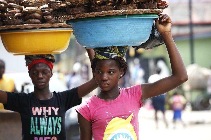 Kemi Olajuwon (right), who at age 12 has to skip school some days to sell smoked fish to help pay for groceries and school fees, joins another girl at work Tuesday in Lagos, Nigeria.