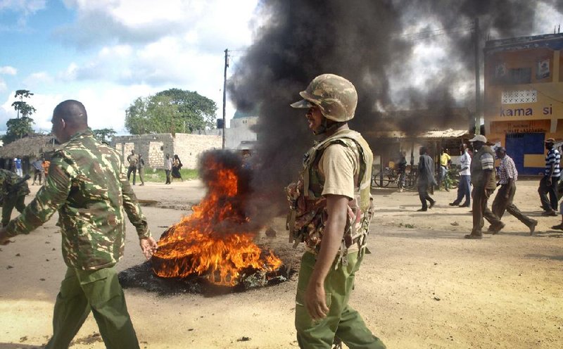 Security forces walk Tuesday past a barricade of burning tires set up by villagers in Kibaoni outside Mpeketoni, Kenya, to protest recent killings and what they said was the government’s failure to provide them security.