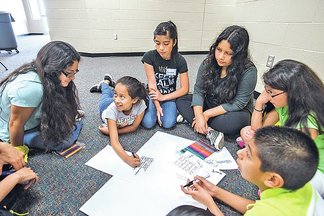 STAFF PHOTO ANTHONY REYES Isela Mercado-Ulloa, left, volunteer with a bilingual summer camp, helps Ruby Pena, 10, and her group find English/Spanish cognates Wednesday at the a bilingual summer camp at J.O. Kelly Middle School in Springdale. The children got a chance to practice their language skills and will learn about and perform community service projects.