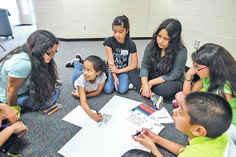 STAFF PHOTO ANTHONY REYES Isela Mercado-Ulloa, left, volunteer with a bilingual summer camp, helps Ruby Pena, 10, and her group find English/Spanish cognates Wednesday at the a bilingual summer camp at J.O. Kelly Middle School in Springdale. The children got a chance to practice their language skills and will learn about and perform community service projects.