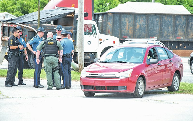 STAFF PHOTO ANTHONY REYES A tow-truck driver moves a red Ford Focus to his truck as Benton County Sheriff&#8217;s Office deputies, Springdale Police and Arkansas State Police gather Wednesday in the parking lot of the Springdale Bowling Alley. The officers arrested the driver of the Focus after a pursuit through Springdale.
